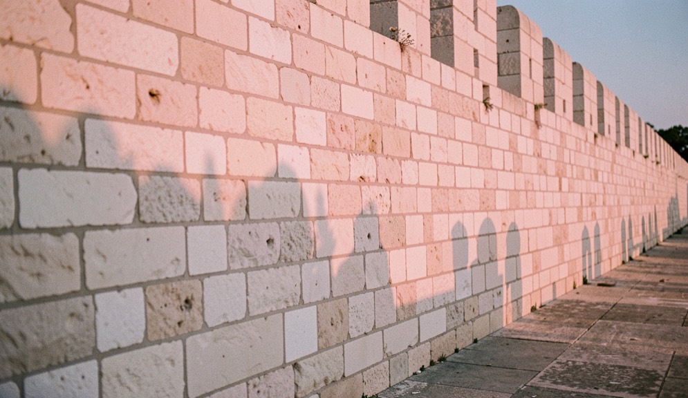 Les murs de la forteresse de Sagres en fin de journée, éclairés de biais par le soleil couchant, avec un cadrage serré sur les joints et les reprises de pierre.
