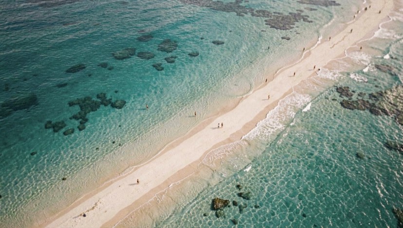 Lagon turquoise vu de haut, un banc de sable clair sépare l'eau peu profonde du bleu profond de l'océan